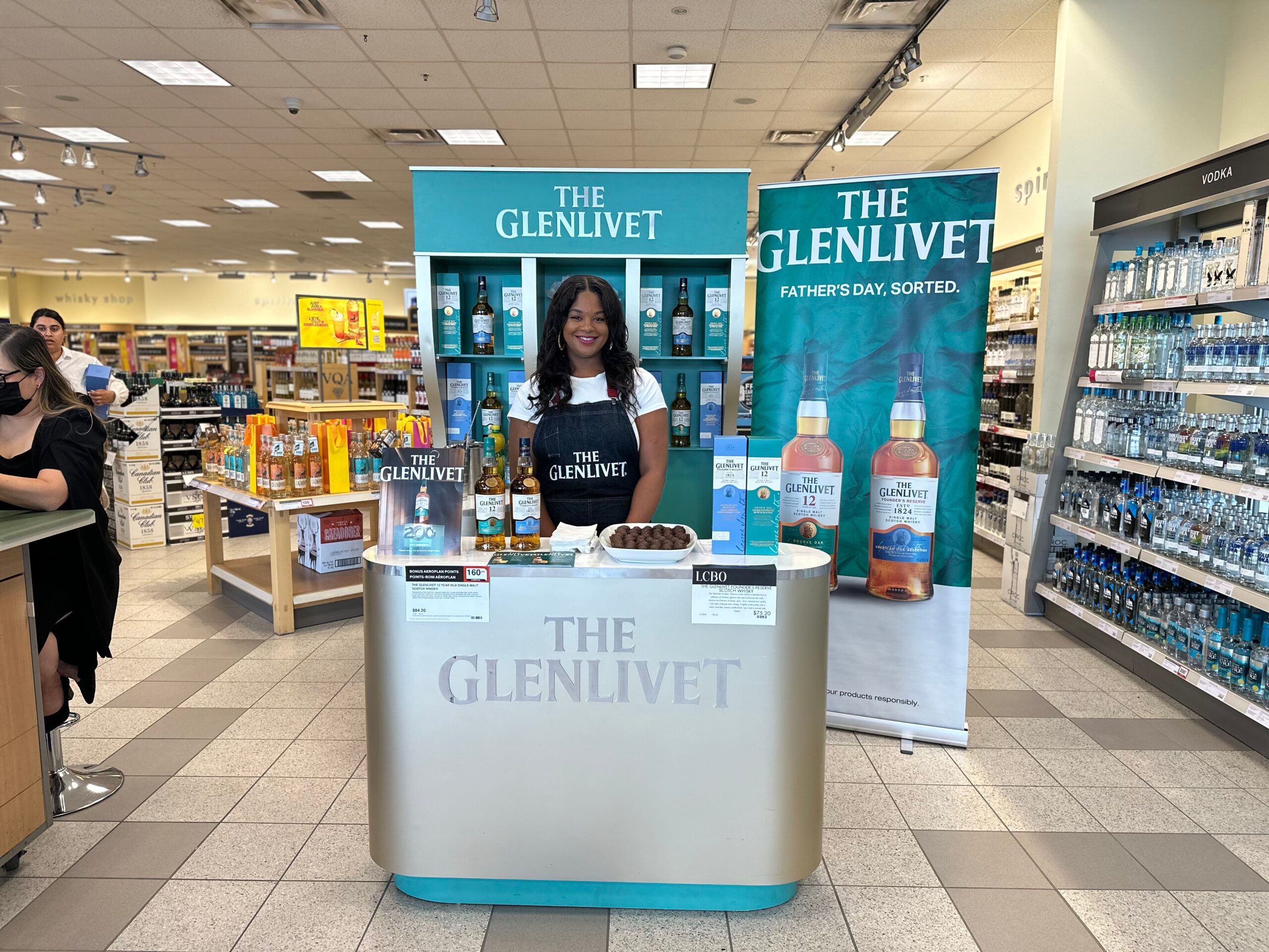 Brand ambassador at a Glenlivet whisky sampling table, showcasing premium whisky bottles and branded materials in a sleek setup.